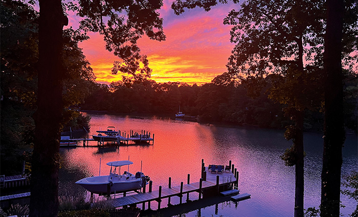 Two docks on a lake amongst various trees kissed by orange and yellow light from a golden sunset.