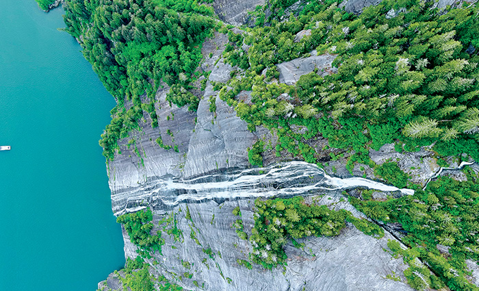 Aerial view of a waterfall with dark green trees and stone.