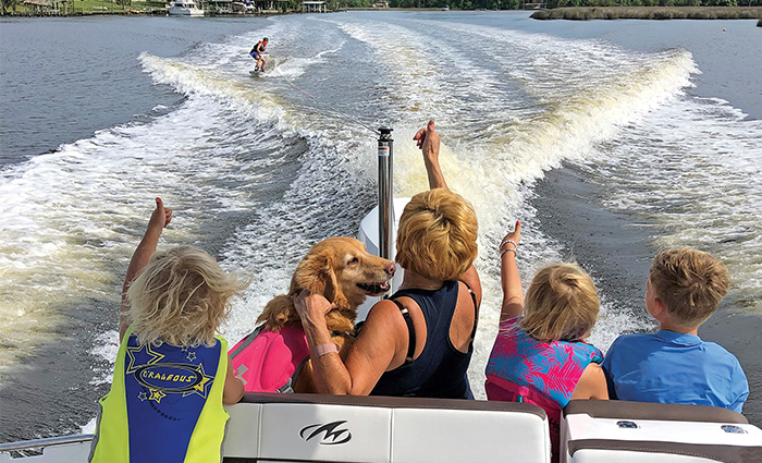 Middle-aged woman, three kids and a golden retriever watching a water skier from the back of a boat.
