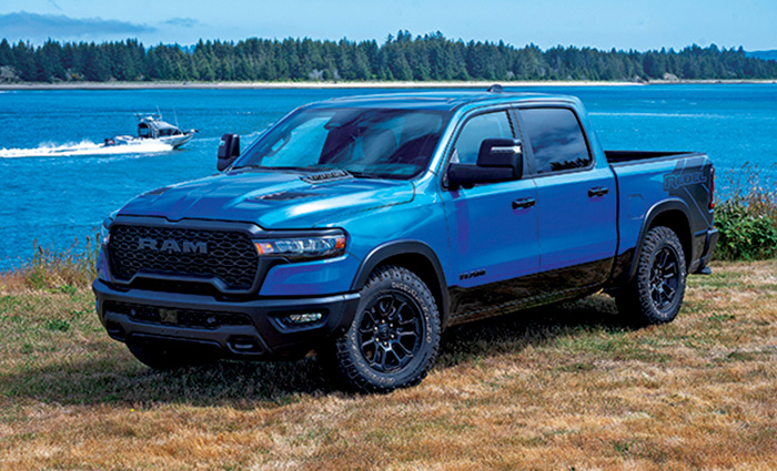Blue Dodge Ram four door truck parked on the shore with a lake and tree line in the background.