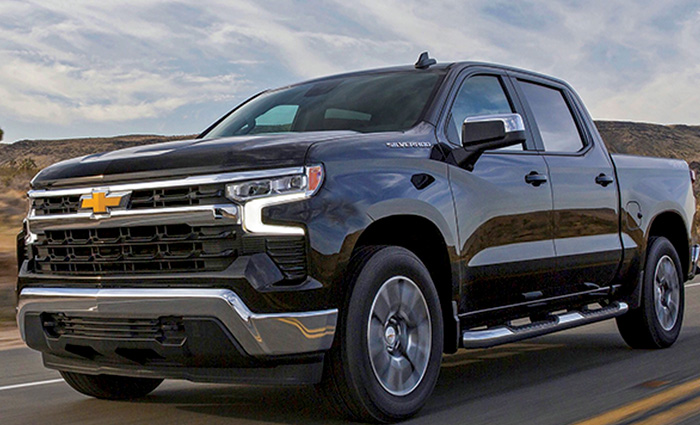 Front view of a black Chevrolet four door truck driving down a two lane highway. 