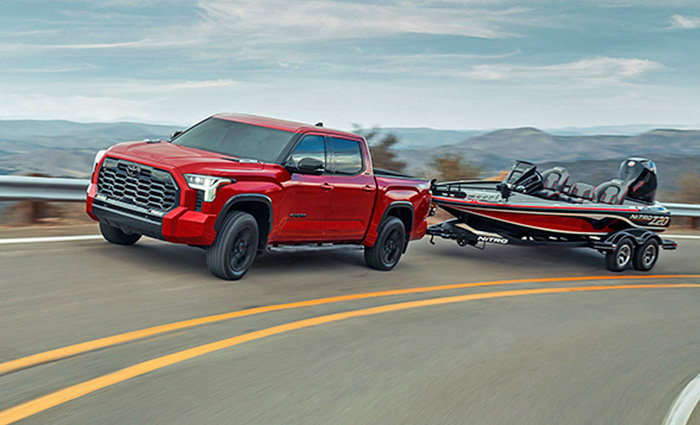 Red Toyota four door truck towing a small black and red fishing truck along a two lane highway.