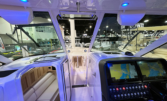 View from the inside of a vessel at an indoor boat show displaying the cabin, steering and navigation, and deck.