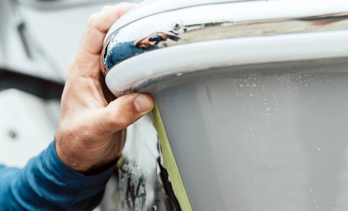 Close up of a Caucasian hand applying a film to a bumper of a white vessel.