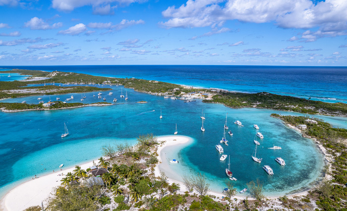 Aerial view of an island featuring sunny skies, big white clouds, green trees and clear blue waters.