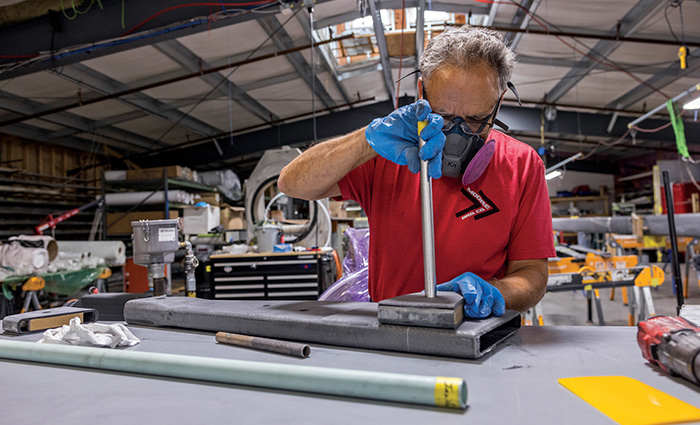 Middle-aged adult male wearing a red shirt, eye glasses and mask working inside a factory.