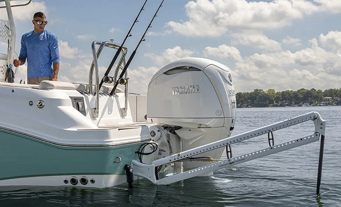 Adult male wearing a light blue long sleeve shirt looking at a large white motor on a white and teel boat.