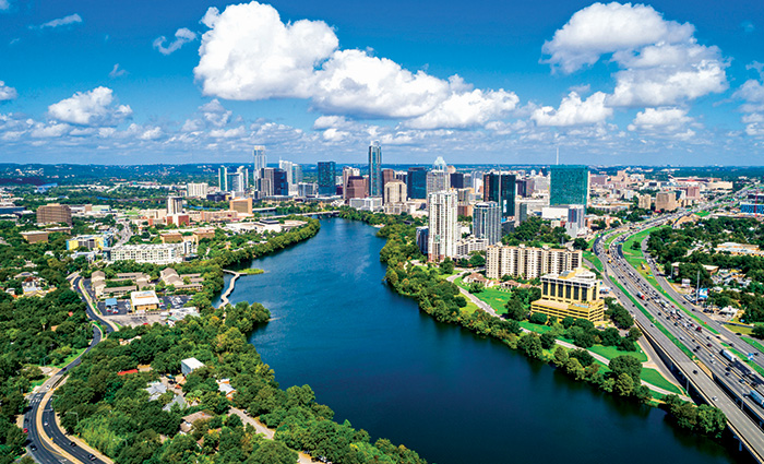 Aerial view of a river with city skyline in the background and fluffy white clouds above. 