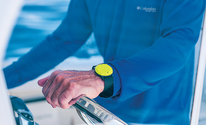 Up-close view of an adult male wearing a long sleeve blue shirt and black watch with bright yellow face steering a boat on the water.