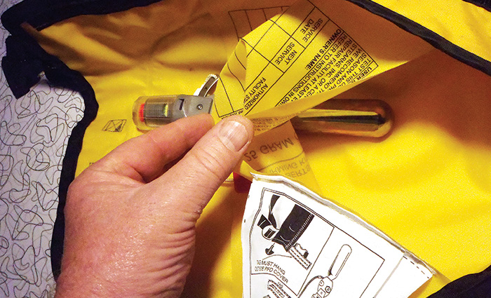 Adult hand holding a white label inside a yellow inflatable life jacket.