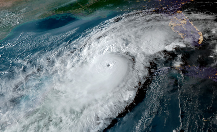 Aerial view of a hurricane showing white clouds circling a coast. 