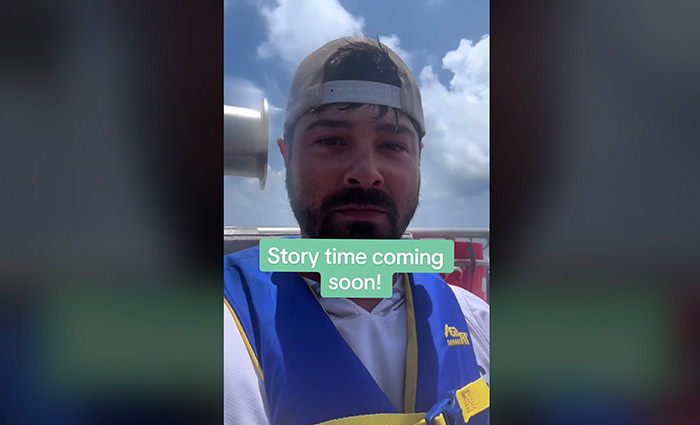 Young adult male wearing backward ballcap and yellow and blue lifejacket taking a selfie on a sunny day.