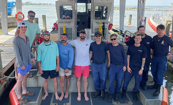 Ten adult males posing for a group photo on a wooden boat dock in front of a rescue boat.