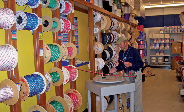Senior adult male wearing a ballcap, navy shirt and khaki pants in front of numerous spool of rope.