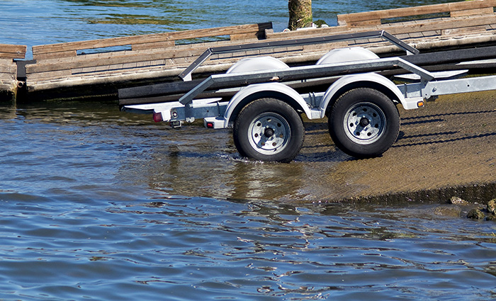An empty white boat trailer with black wheels and white rims backing into water.