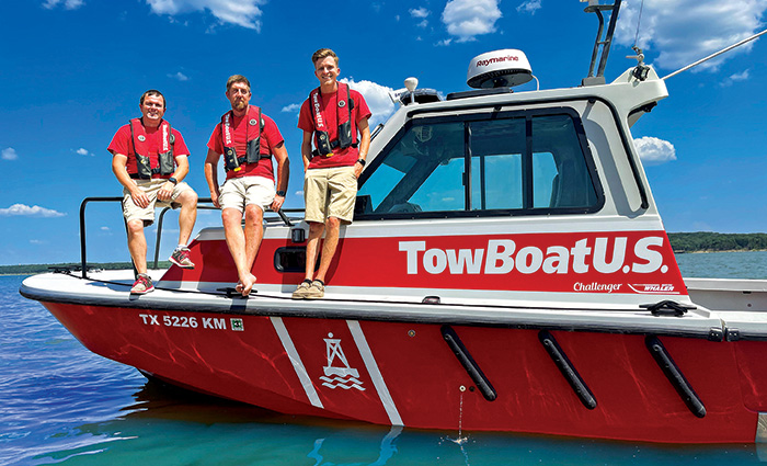 Three young adult males wearing red shirts and khaki pants posing for a photo aboard a red and white tow boat on open waters.