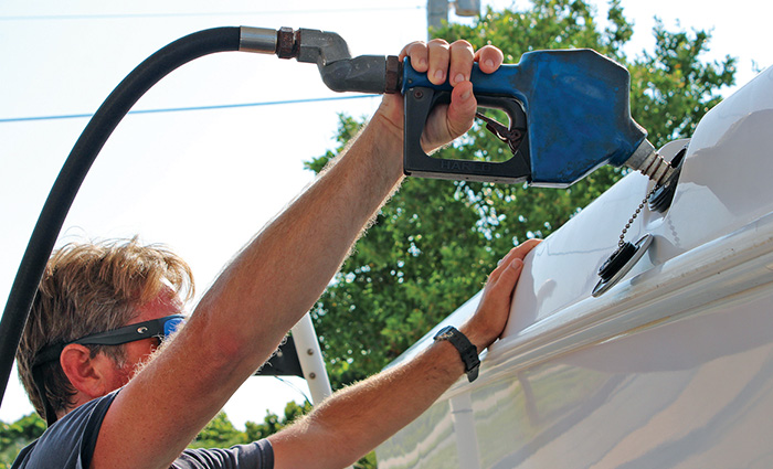Adult male wearing black sunglasses with blue lenses holding a blue nozzle and fueling a white boat.