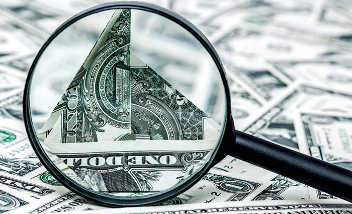 Black magnifying glass providing a closer view of a dollar bill amongst countless other bills.