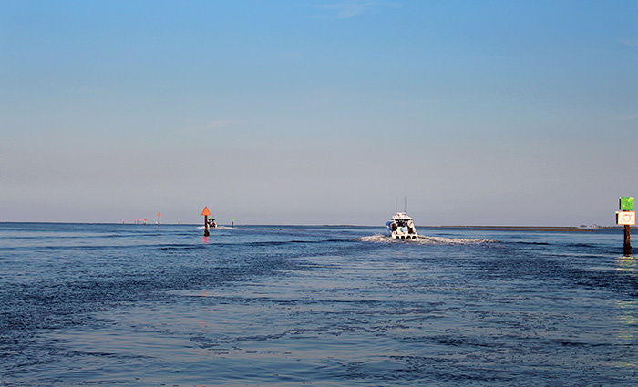 View from behind of a large white vessel on open waters navigating into the sunset.