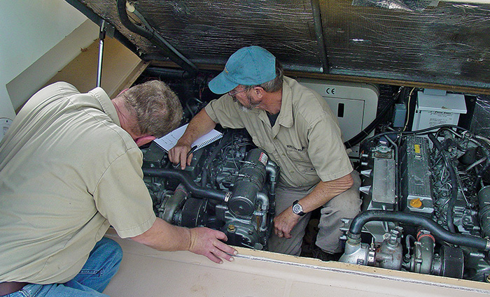 Two men, both wearing tan button up shirts, repairing a large engine.