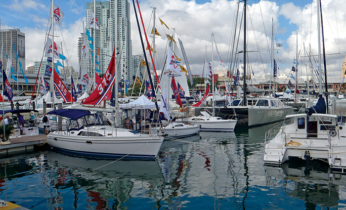Numerous white vessels aligned at a marina with large buildings and white clouds in the background.