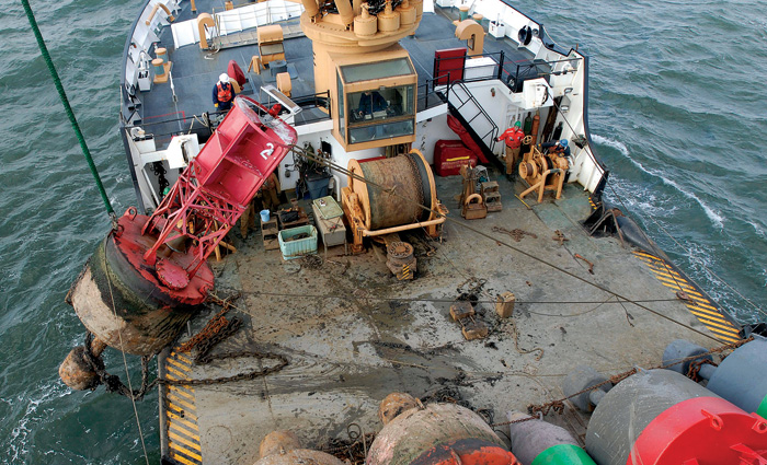 Large red buoy being pulled from the water by a large yellow crane on a vessel.