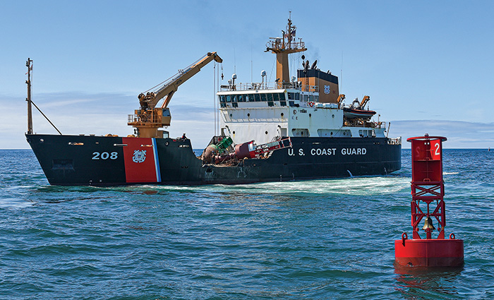 Large red buoy in blue waters with a black, red and white vessel in the background.