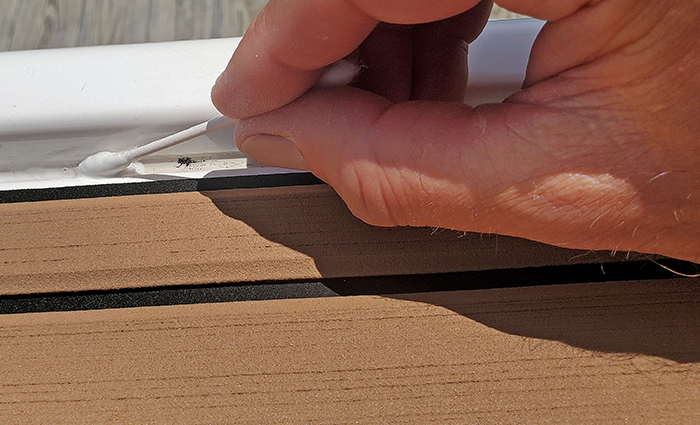 Up-close view of a hand with a cotton swab cleaning a boat's caulk line.