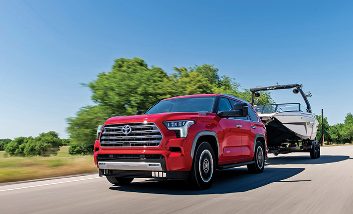 Red Toyota SUV pulling a white and black boat in a trailer cruising down a highway.