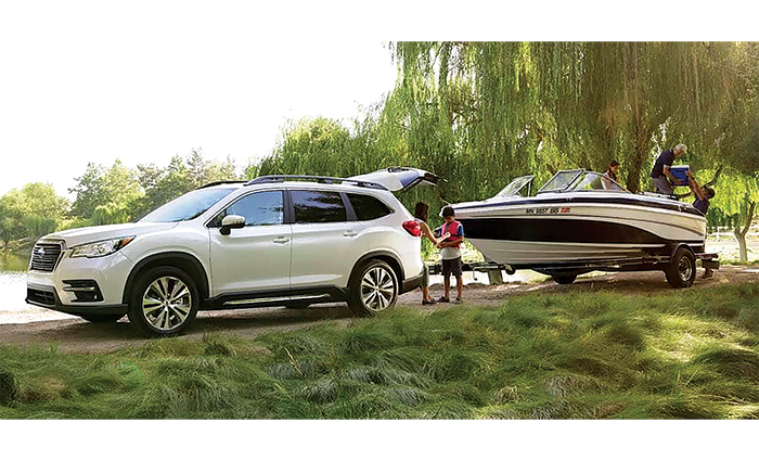 White 2026 Subaru Crosstrek Hybrid parked alongside a pond with a white and blue boat on its tow.
