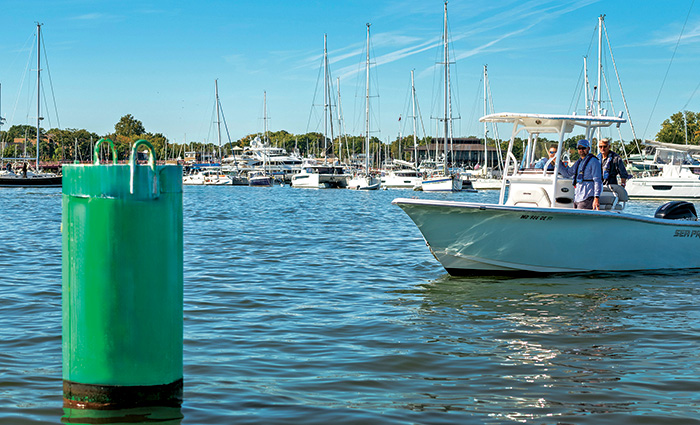 Green buoy with small white boat and marina in the background.