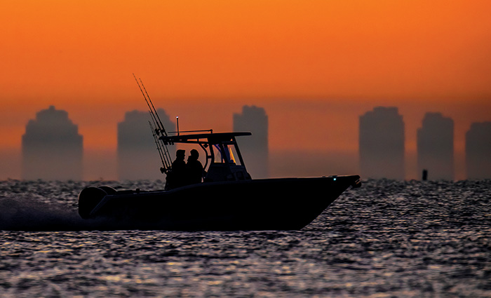 Orange sunset with skyline, vessel and sparkling open waters in the foreground.  