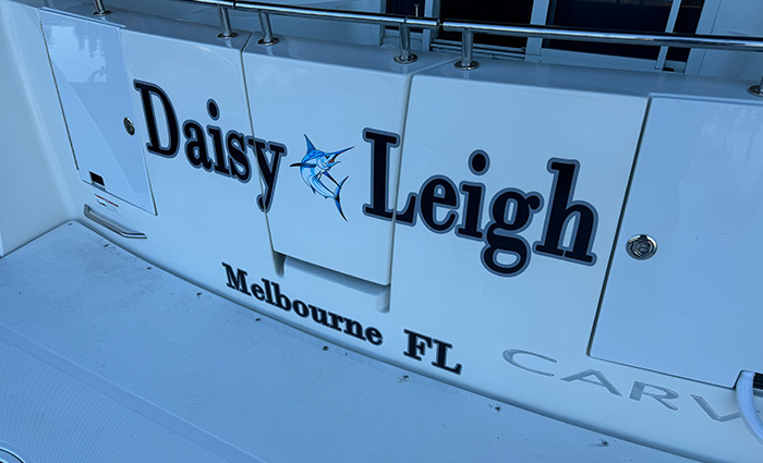 Back of a white boat with navy blue lettering reading 'Daisy Leigh'