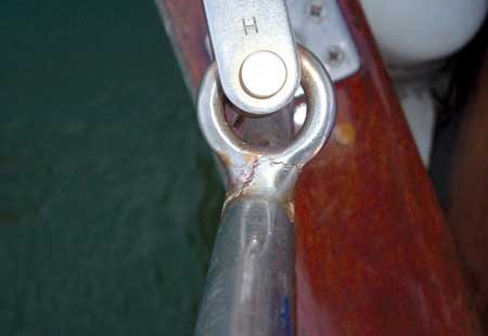 close up of a stainless steel object with the letter 'H' imprinted. Second circular piece connected to it. Both items mounted to a wooden structure.