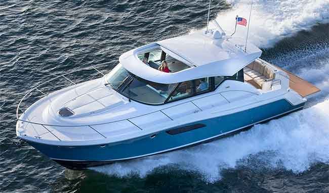 Aerial view of large blue and white powerboat underway at sea. American flag blowing off top of back of boat. Woman in red shirt visible inside of boat.